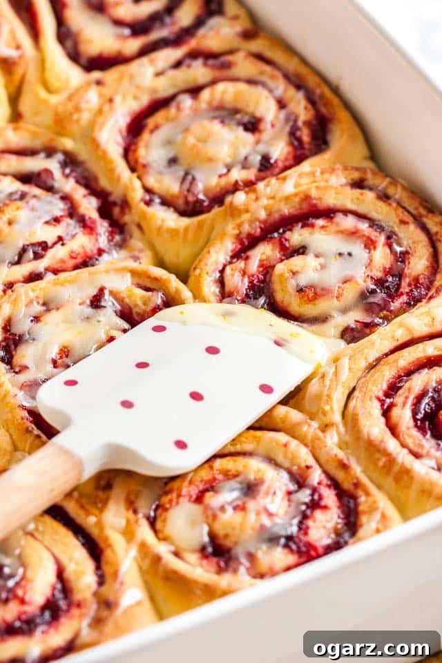 Zesty Cranberry Orange Buns 3 A white baking dish with orange cranberry rolls with sweet orange glaze with a white and red polka dot spatula on them.