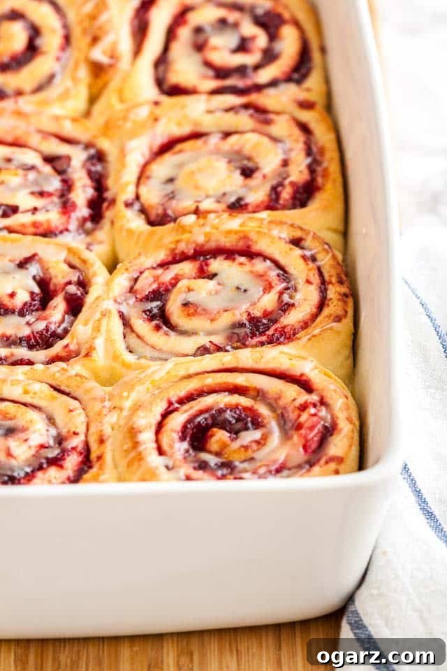 Zesty Cranberry Orange Buns 7 A white baking dish with orange cranberry rolls on a bamboo cutting board with a white and blue dishtowel.