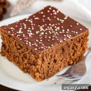 A white plate featuring a square of chocolate topped spice cake with a fork, poised for tasting.