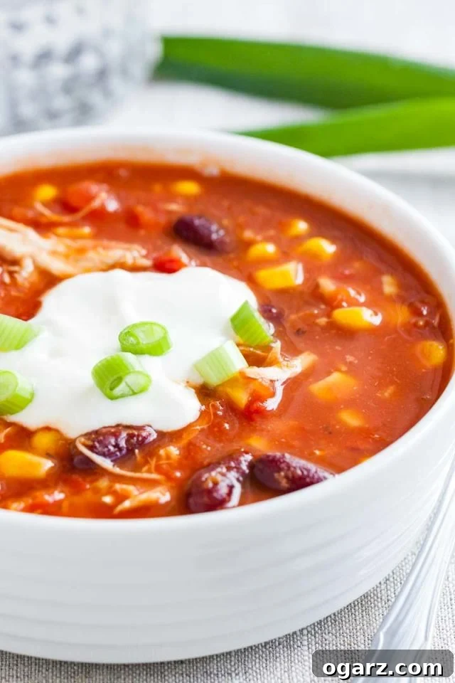 Close up of a white bowl with chicken chili, topped with sour cream and chives.