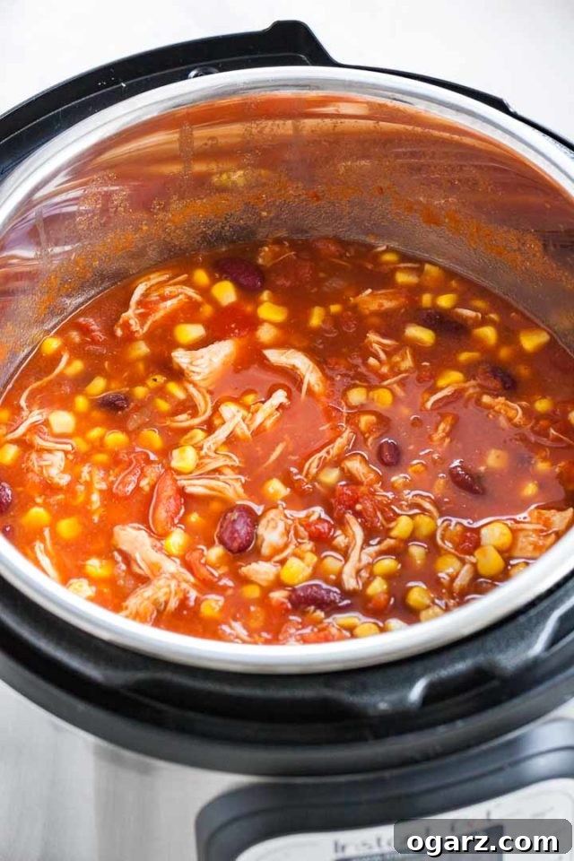 An instant pot with chicken chili containing shredded chicken, pinto beans and corn.