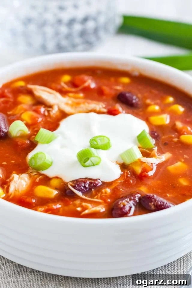 Close up of a white bowl with chicken chili, topped with sour cream and chives.