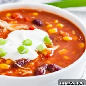 Close up of a white bowl with chicken chili, topped with sour cream and chives.