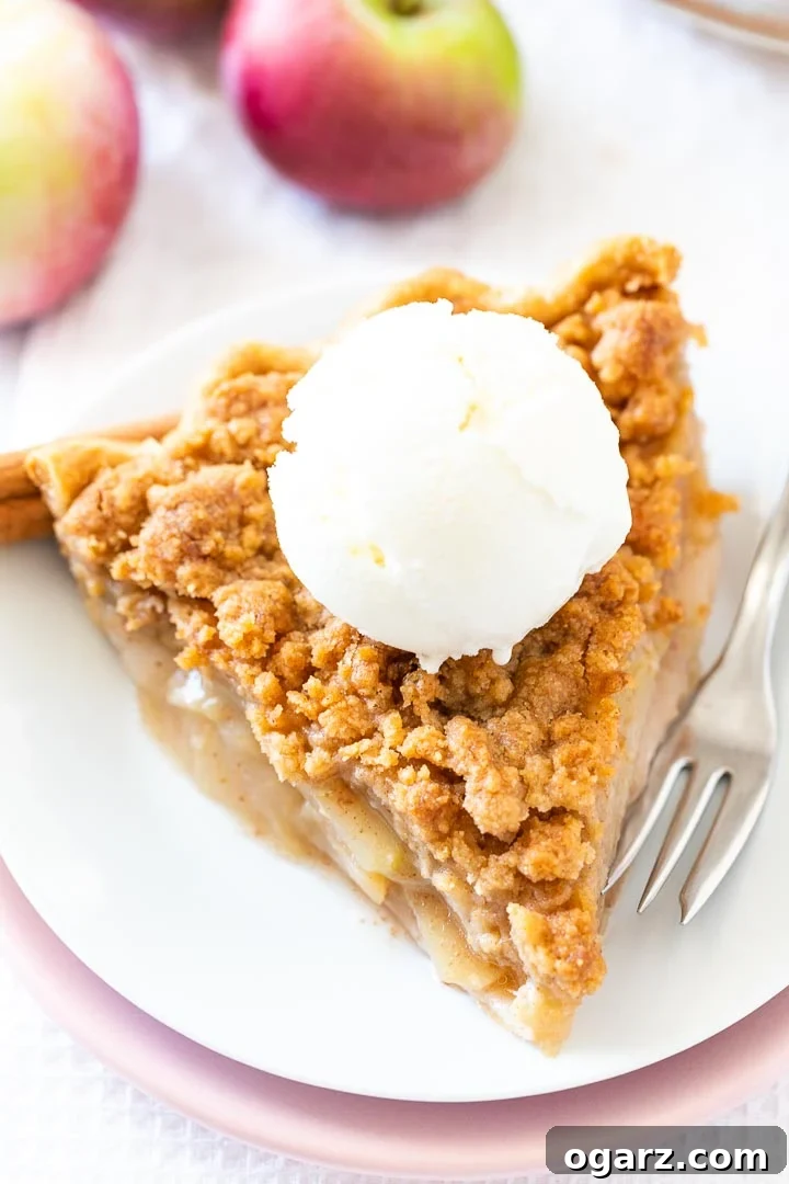 Ultimate Apple Crumble Pie 2 A perfectly baked slice of Apple Crumble Pie, featuring a golden streusel topping and warm apple filling, served on a white plate with a scoop of vanilla ice cream, garnished with cinnamon sticks and a fresh apple slice.