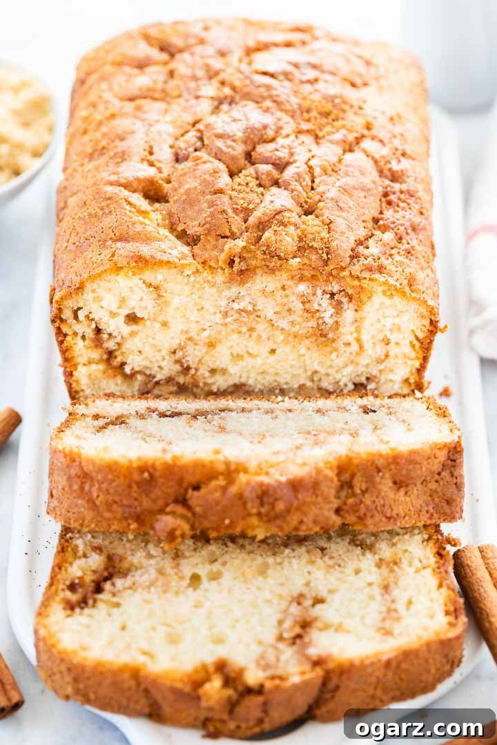 Cinnamon Swirl Bread is so easy to make without yeast and has a delicious cinnamon sugar swirl inside and a crunchy cinnamon sugar crust on top. This moist homemade Cinnamon Bread tastes delicious for breakfast but also makes a great afternoon snack! A quick bread that's perfect for the holidays and keeps fresh for days. #cinnamon #cinnamonswirlbread #cinnamonbread #quickbread #holidaybaking #recipe A cinnamon swirl bread on a white rectangular serving platter, with 2 slices cut off and lying down garnished with cinnamon sticks.