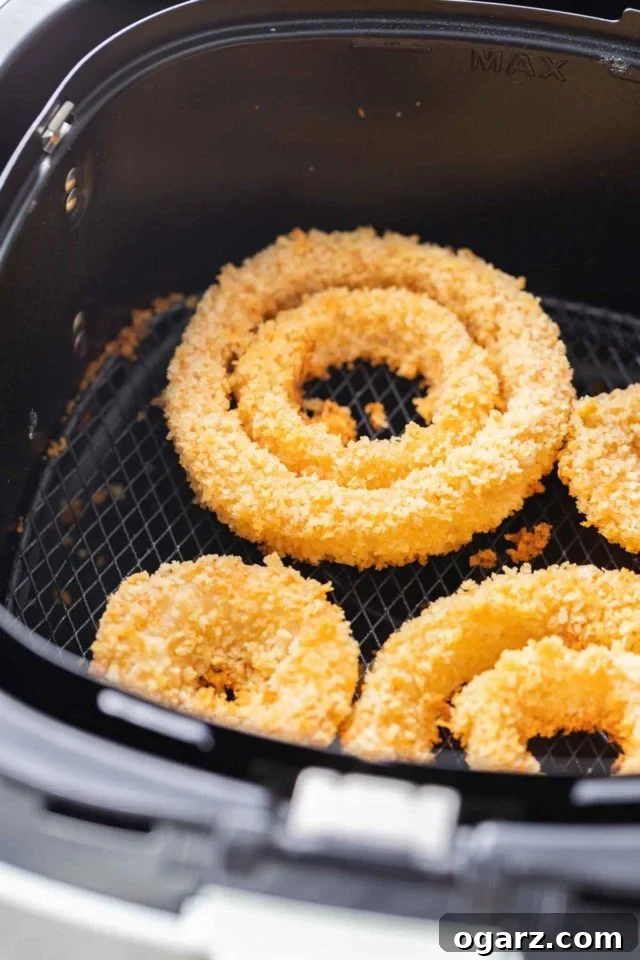 A single layer of golden-brown air fryer onion rings in an air fryer basket.
