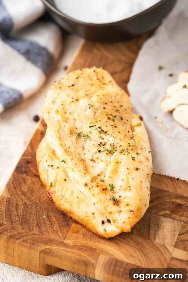 Juicy Air Fryer Chicken Breast rubbed with a simple seasoning and air fried to perfection. This easy and quick chicken breast recipe is perfect for meal prep, salads, and sandwiches! #AirFryerRecipes #BakedChickenBreast A perfectly grilled chicken breast garnished with fresh herbs, alongside some neatly sliced chicken, on a dark wood cutting board with a white and blue dish towel.