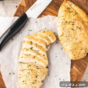 Two perfectly cooked, juicy air fryer chicken breasts on a dark wood cutting board with parchment paper, one sliced to reveal its tender interior.