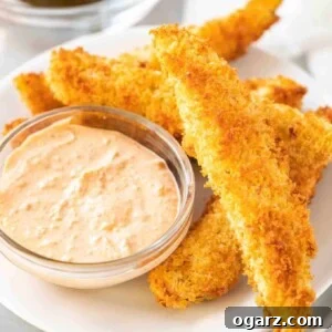 A heap of air fryer dill pickles on a white plate with a small glass bowl with a dip in it.