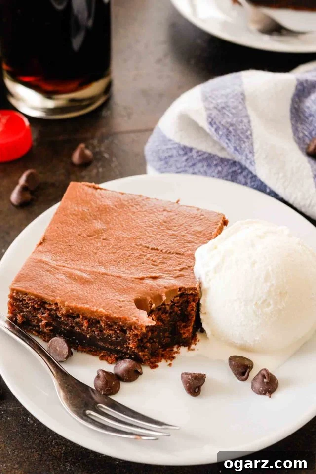 slice of coca-cola cake on a white plate with vanilla ice cream, a fork, and some chocolate chips with a bite taken out of it
