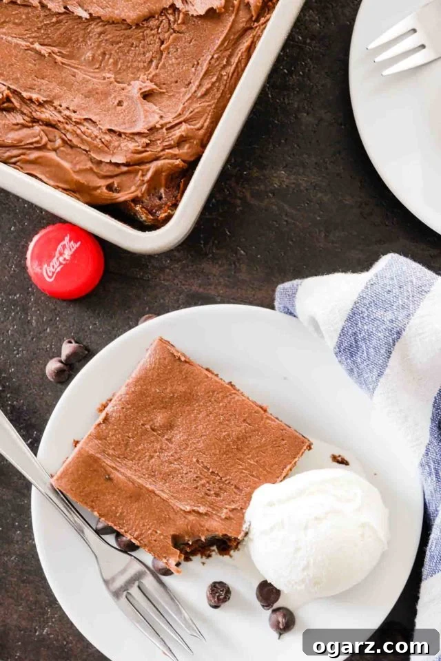 top-down shot of coca cola cake on a white plate with vanilla ice cream, the corner of a baking sheet with the cake in it and a bottle cap on a dark table.