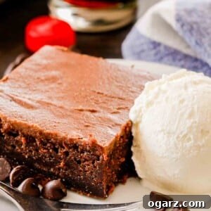slice of coca-cola cake on a white plate with vanilla ice cream, a fork, and some chocolate chips with a white and blue dish towel and a coca-cola bottle cap in the background