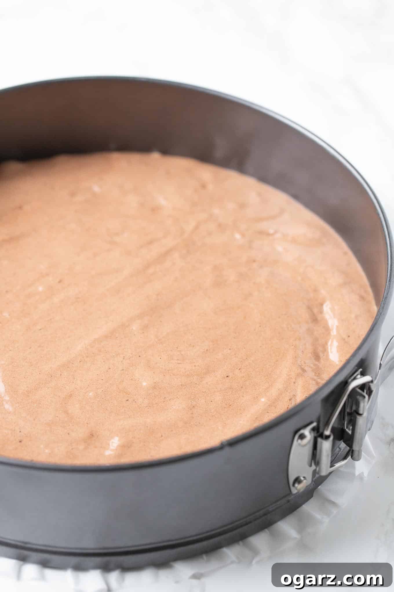 Dark Forest Cherry Delight 7 Light chocolate cake batter evenly spread in a parchment-lined springform pan, ready for baking.