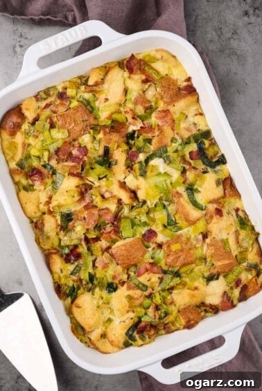 A white oblong casserole with handles filled with freshly baked savory bread pudding with bacon and leeks, a perfect make-ahead brunch dish.