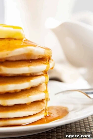 A side view of a stack of fluffy pancakes on a white plate, topped with a thick pat of butter and a drizzle of maple syrup, inviting guests to a delicious brunch.