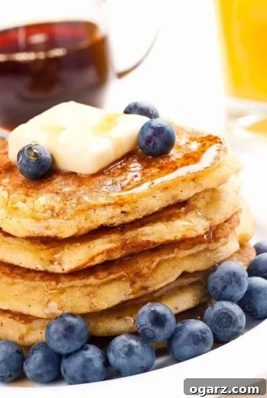 A stack of cornmeal pancakes on a plate, topped with fresh blueberries and a pat of butter, and drizzled with maple syrup, creating a visually appealing brunch option.