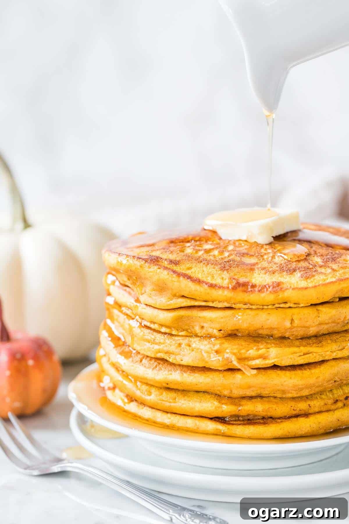 A stack of golden Pumpkin Pancakes with melting butter and a generous drizzle of maple syrup, garnished with a sprinkle of pumpkin pie spice.