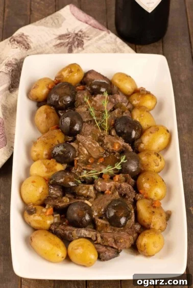 A serving platter of sliced slow-cooker pot roast surrounded by braised mushroom caps and baby potatoes, garnished with a sprig of fresh thyme.