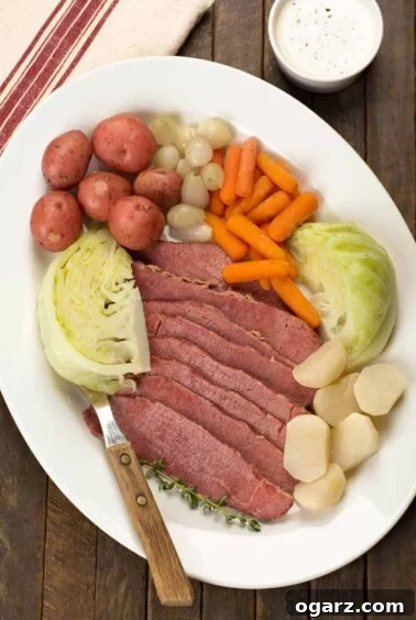 A serving platter with New England boiled dinner; sliced corned beef brisket, cabbage wedges, baby red potatoes, baby carrots, pearl onions, and turnips.