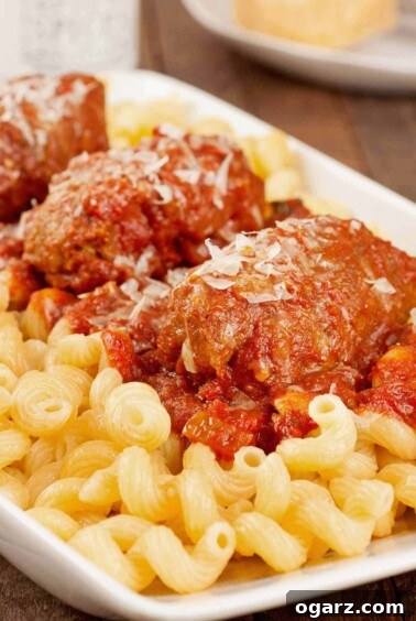 Close up photo of slow-cooked Italian beef braciole served with tomato and red wine sauce over pasta.