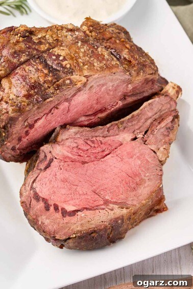 A succulent prime rib roast, beautifully browned and partially carved, rests on a white serving platter, accompanied by a side of classic horseradish cream sauce.