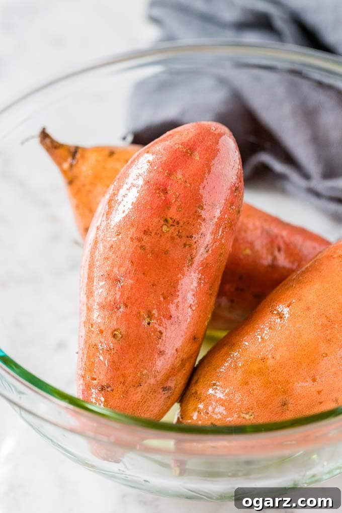 Perfect Air Fryer Sweet Potatoes 3 A glass bowl with raw, whole sweet potatoes, covered with olive oil.