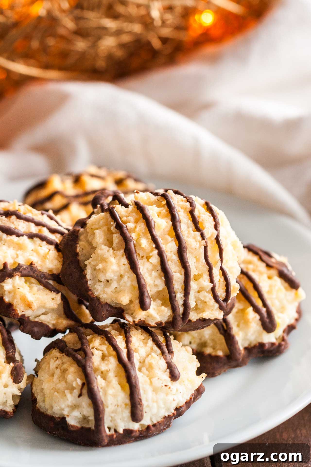 Irresistible Homemade Coconut Macaroons 3 Delicious coconut macaroons, some with rich chocolate bottoms and elegant chocolate stripes, arranged neatly on a pristine white plate beside a soft white dishtowel, ready to be enjoyed.