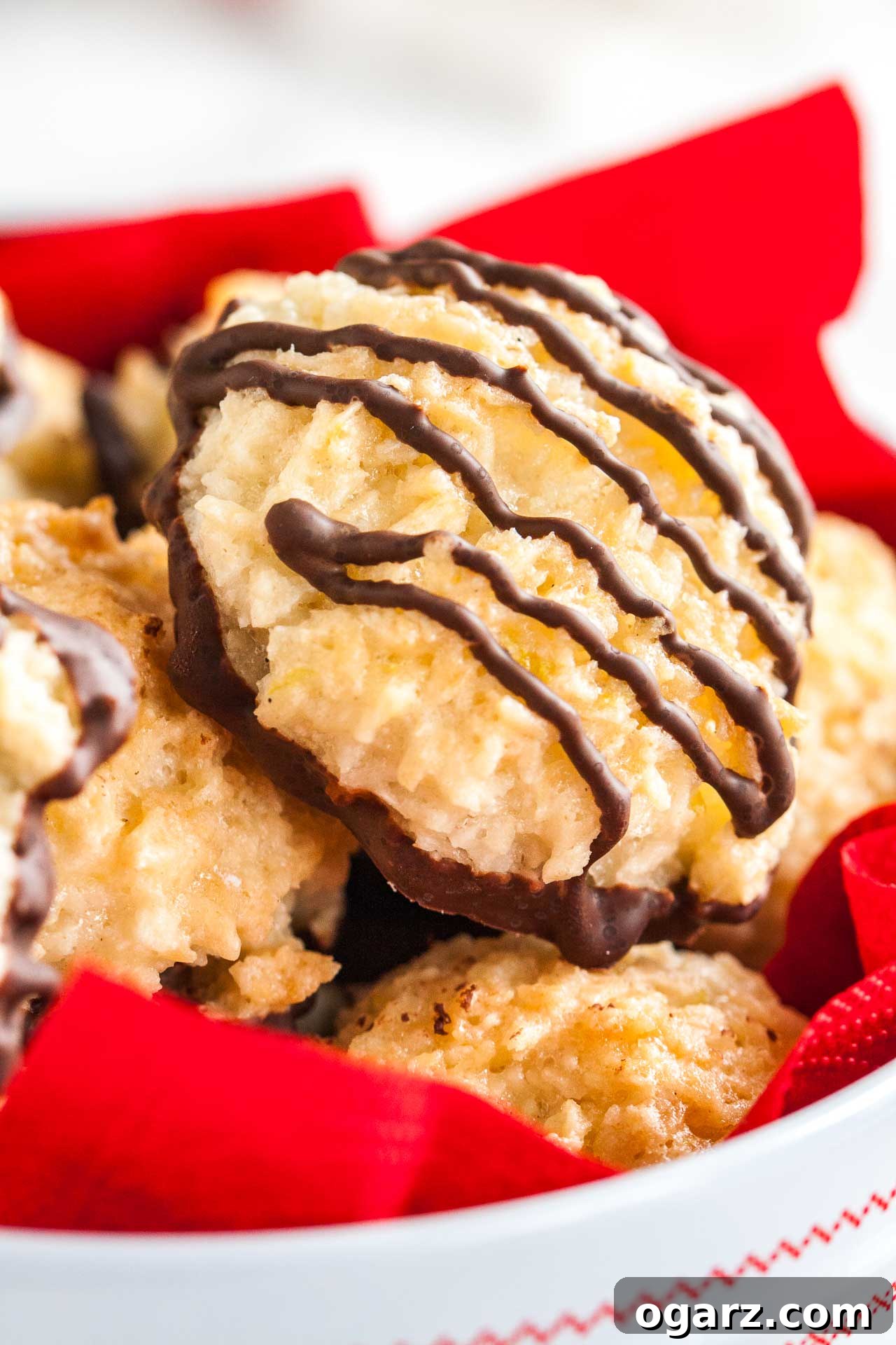 Irresistible Homemade Coconut Macaroons 4 A detailed close-up shot of a white cookie box, beautifully lined with a vibrant red napkin, filled with an assortment of homemade coconut macaroons, highlighting their texture.