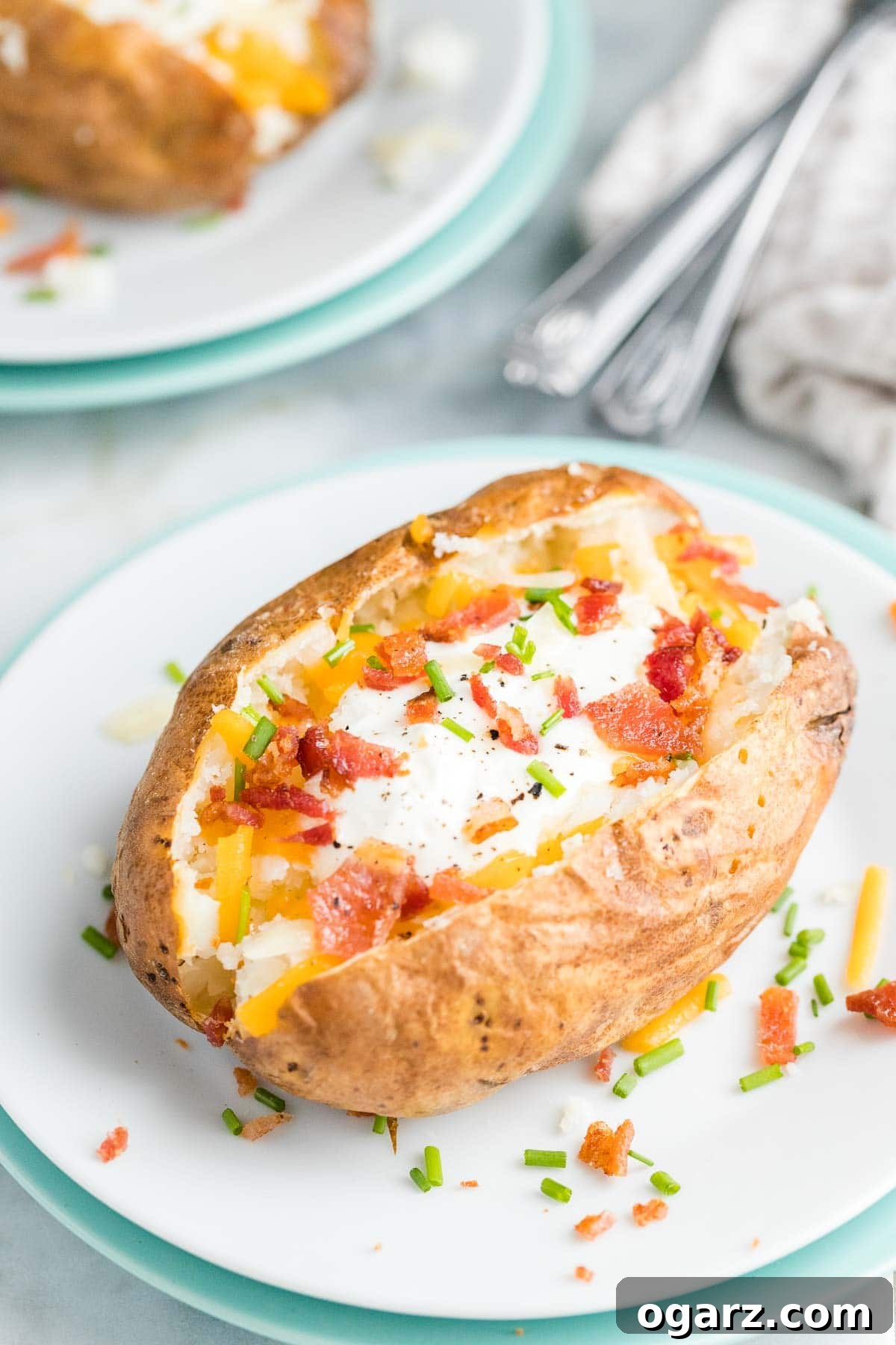 An air fried baked potato garnished with sour cream, bacon, and cheese on a white plate, ready to be enjoyed.