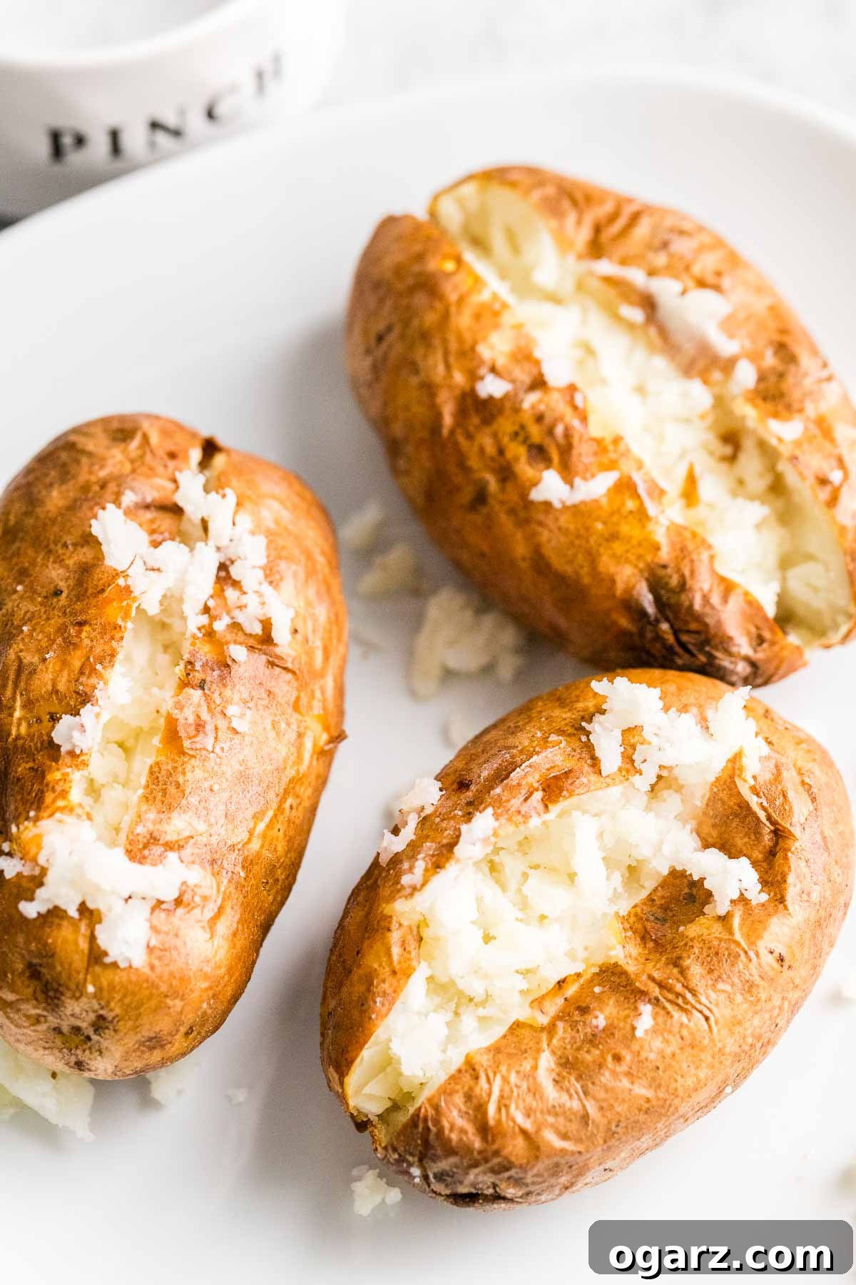 Baked potatoes cut open and fluffed with a fork on a white plate, showcasing their fluffy interior.