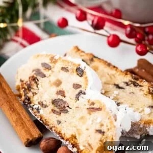 Traditional German Christmas Stollen 4 Two slices of christstollen on a white plate garnished with cinnamon sticks, cranberries and hazelnuts.