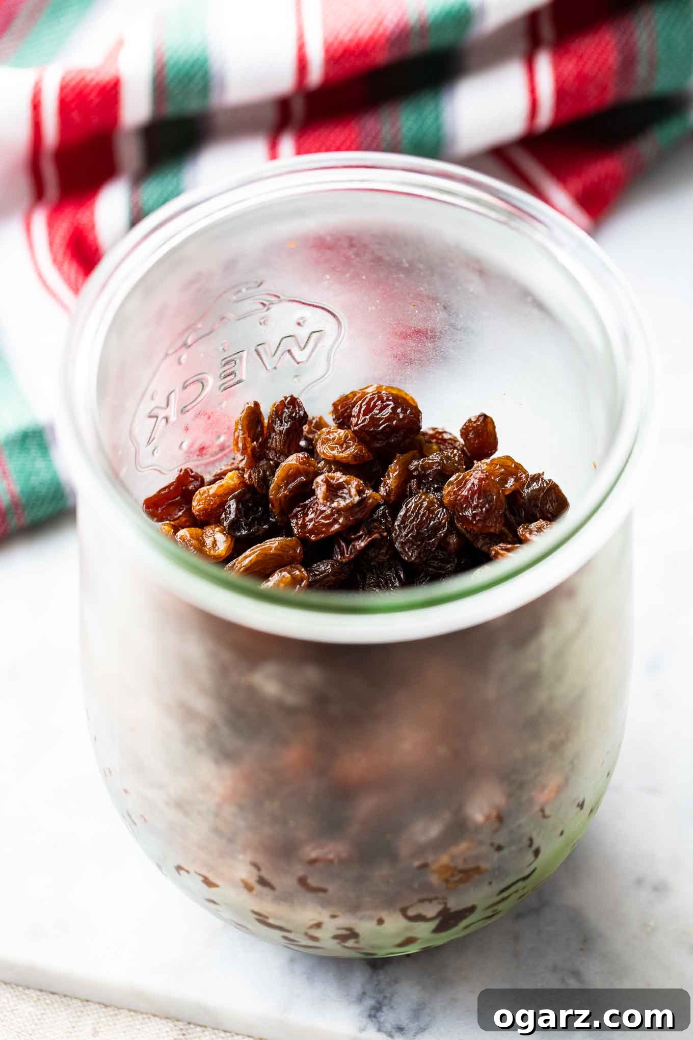 Traditional German Christmas Stollen 3 A Weck jar filled with plump raisins next to a festive red, white, and green dish towel, ready for Stollen preparation.