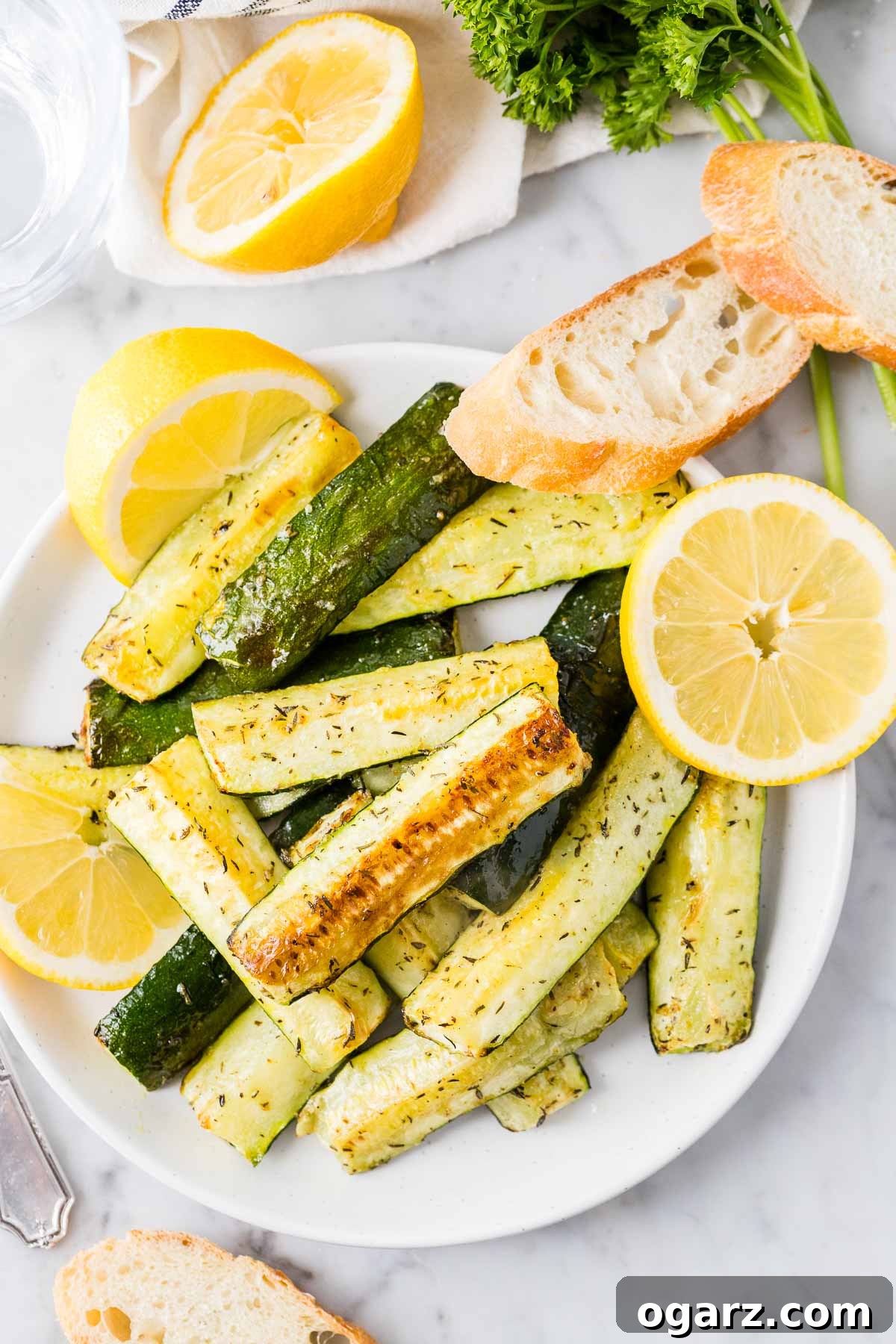 Crispy Air Fryer Zucchini spears on a white plate, garnished with fresh lemon slices and a sprinkle of herbs.