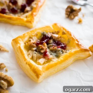 Pear Gorgonzola Mini Tartlets 6 Pear and gorgonzola mini tartlets with cranberry sauce on white parchment paper garnished with walnuts and with a spoon next to it.
