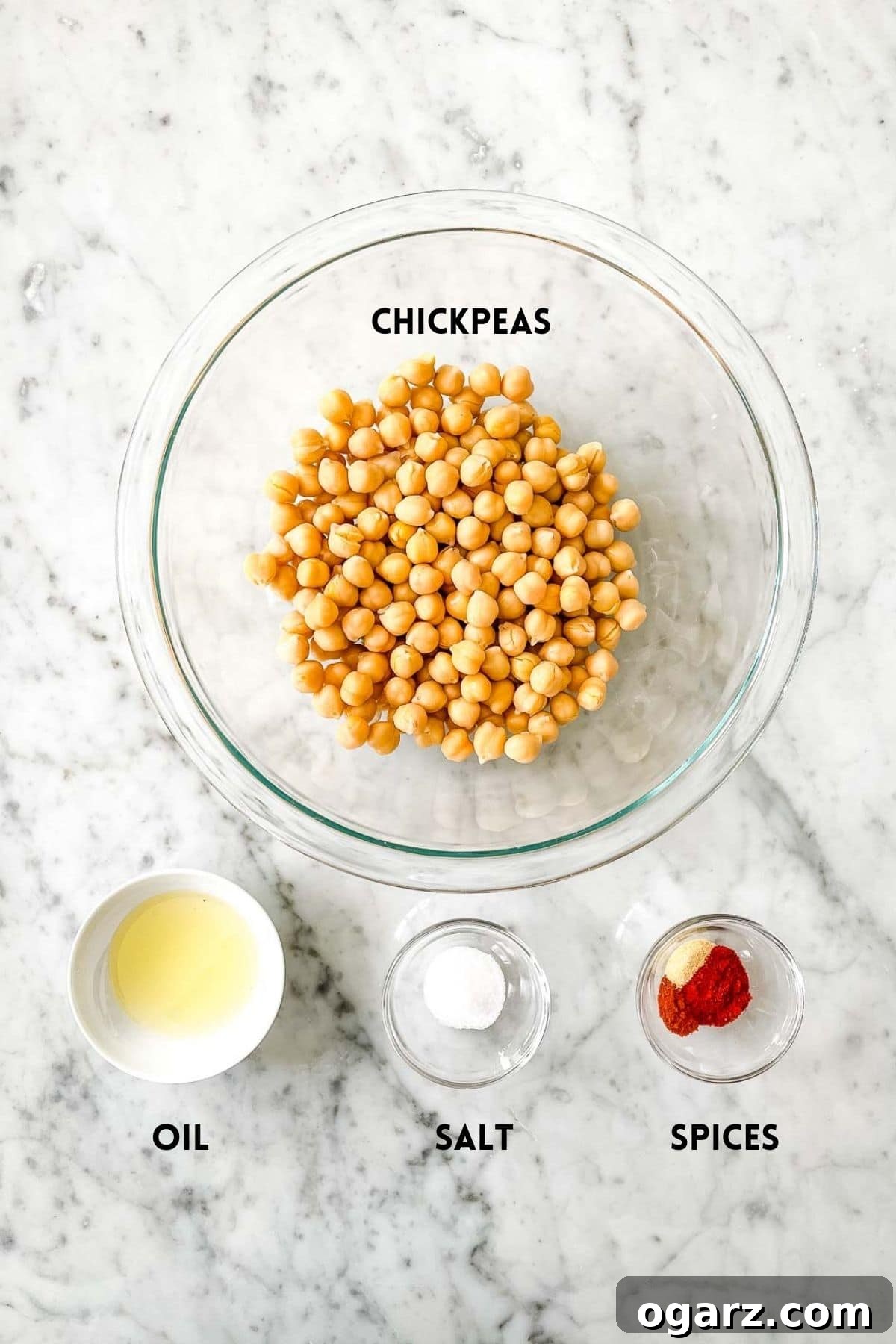 A flat lay photograph showcasing the simple ingredients required for air fryer chickpeas: a can of chickpeas, a bottle of olive oil, and various spices arranged in small bowls.