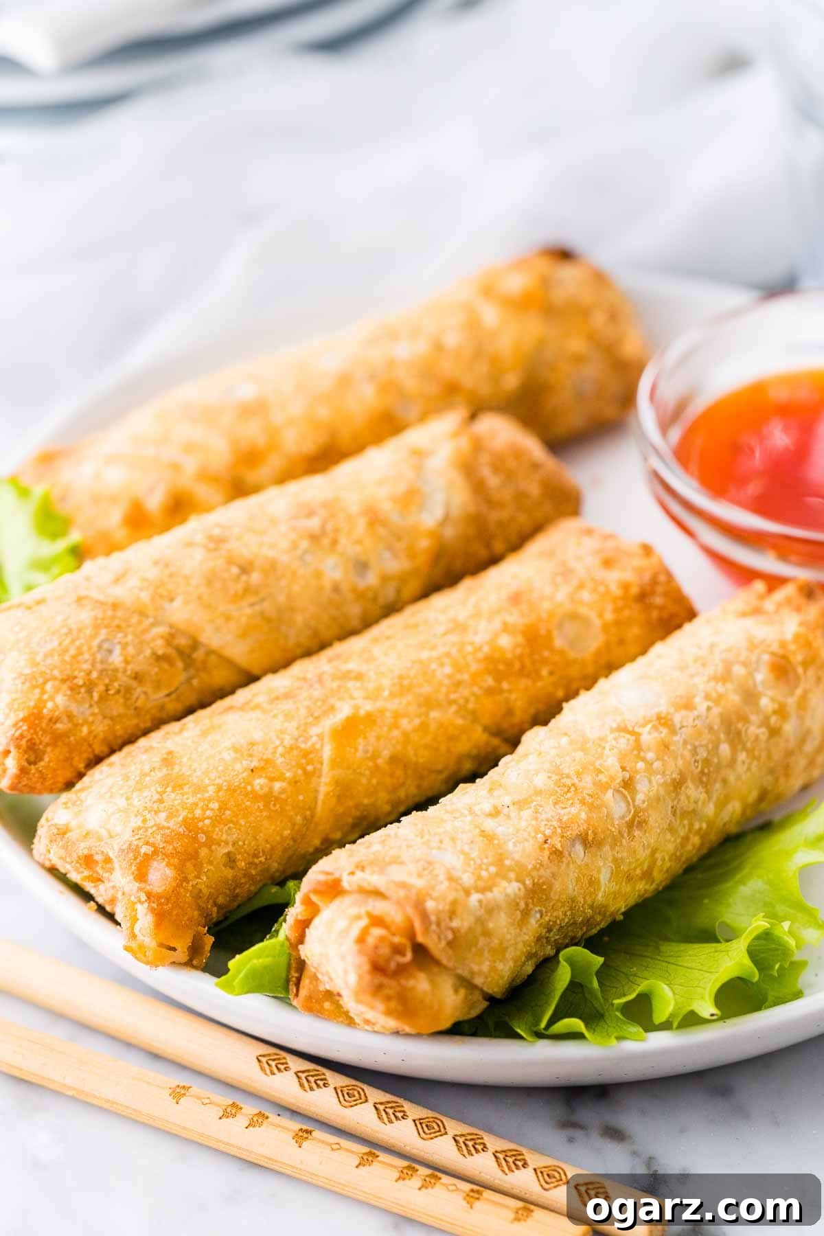 Crispy Air Fryer Egg Rolls 2 Crispy Air Fryer Frozen Egg Rolls on a white plate next to a bowl of sweet and sour sauce.