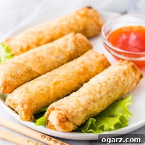 Crispy Air Fryer Egg Rolls on a white plate next to a bowl of sauce.