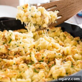 A cast-iron pan with cheese spaetzle. A slotted spatula is lifting out a portion.