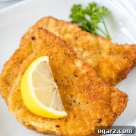Two fried Schnitzels on a white plate, garnished with a wedge of lemon and parsley