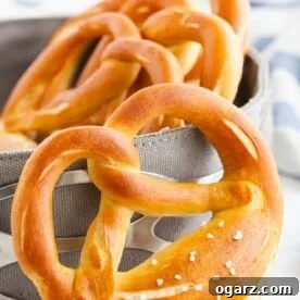 A pretzel leaning against a bread basket, containing more pretzels with a white and blue dish towel in the background.