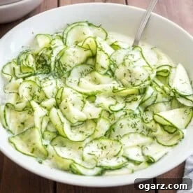 German Cucumber salad in a white salad bowl on a wooden table with a spoon in it