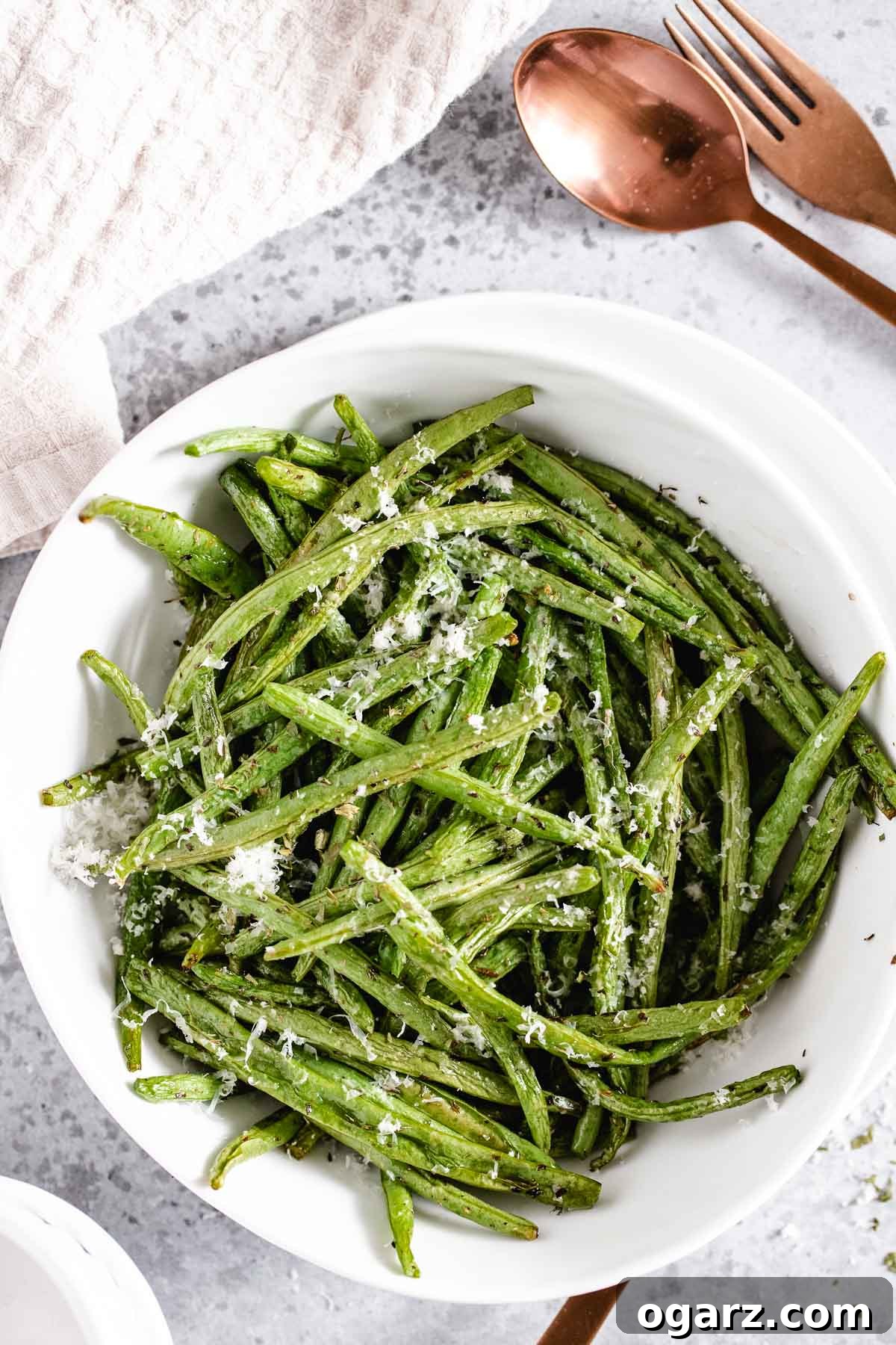 Crispy Air Fryer Green Beans 5 Top-down shot of a white bowl filled with perfectly air-fried green beans, artfully arranged on a clean grey background.