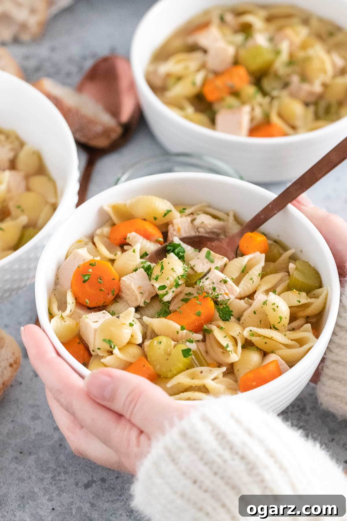 female hands holding a bowl of soup with a spoon sticking out of it