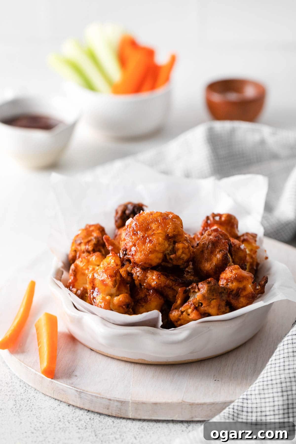 Crispy Air Fryer Cauliflower Bites 6 A wooden board showcasing a bowl of cauliflower wings, garnished with fresh herbs, alongside some vibrant carrots.