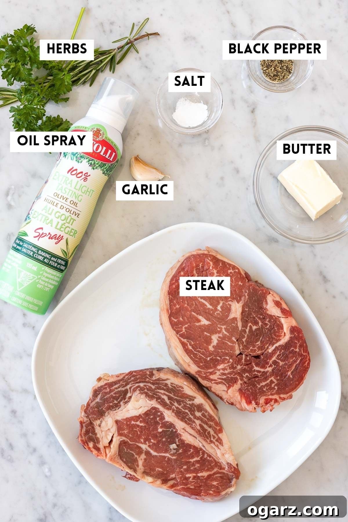 Ingredients for making steak, including raw ribeye, olive oil, and herbs.