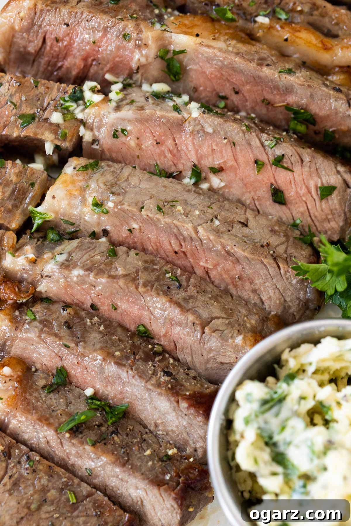 A sliced medium-cooked steak next to a small bowl of garlic butter, ready to be served.