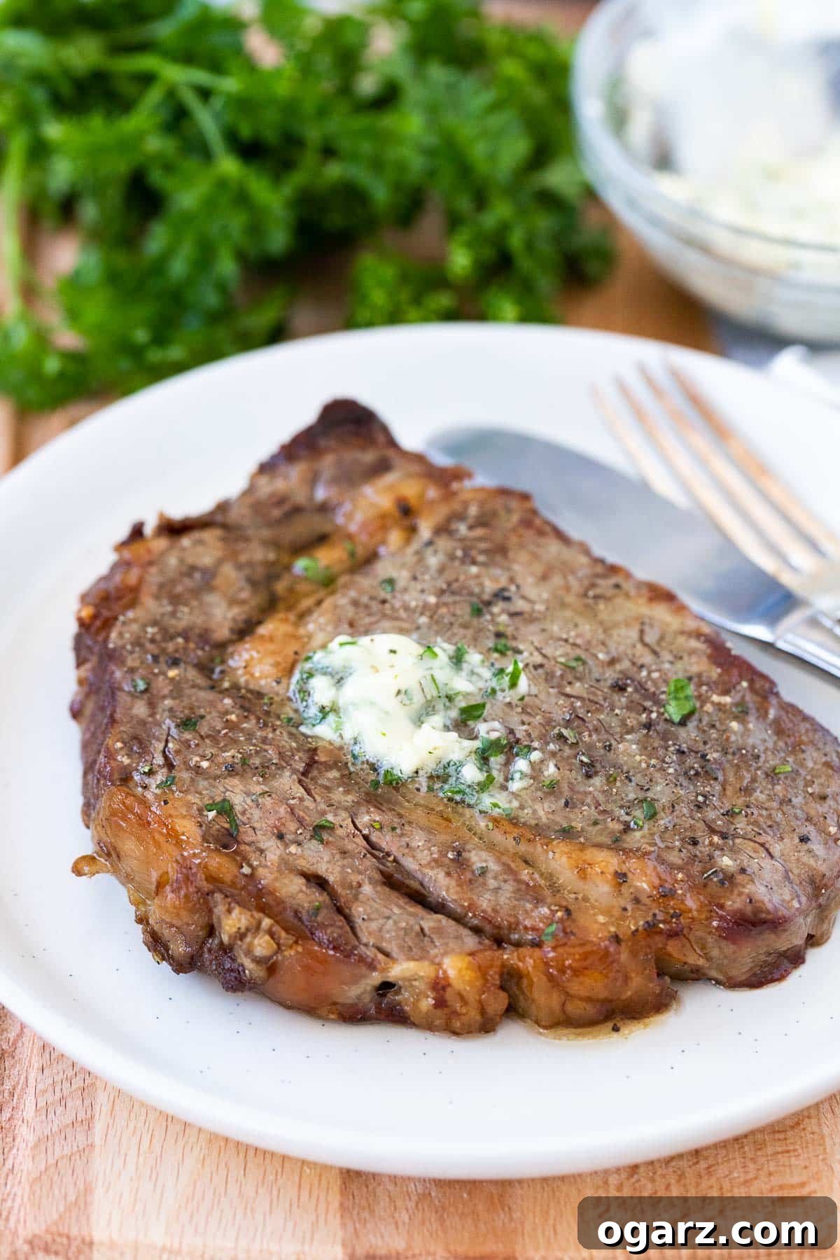 A cooked steak on a white plate with a fork and knife next to it, ready to be enjoyed.