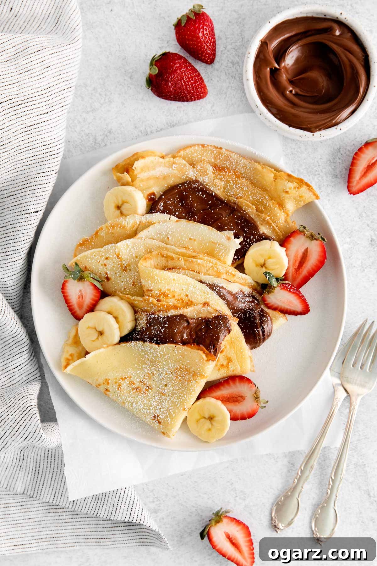 Effortless French Crepes 2 French crepes folded and filled with Nutella on a plate, garnished with powdered sugar