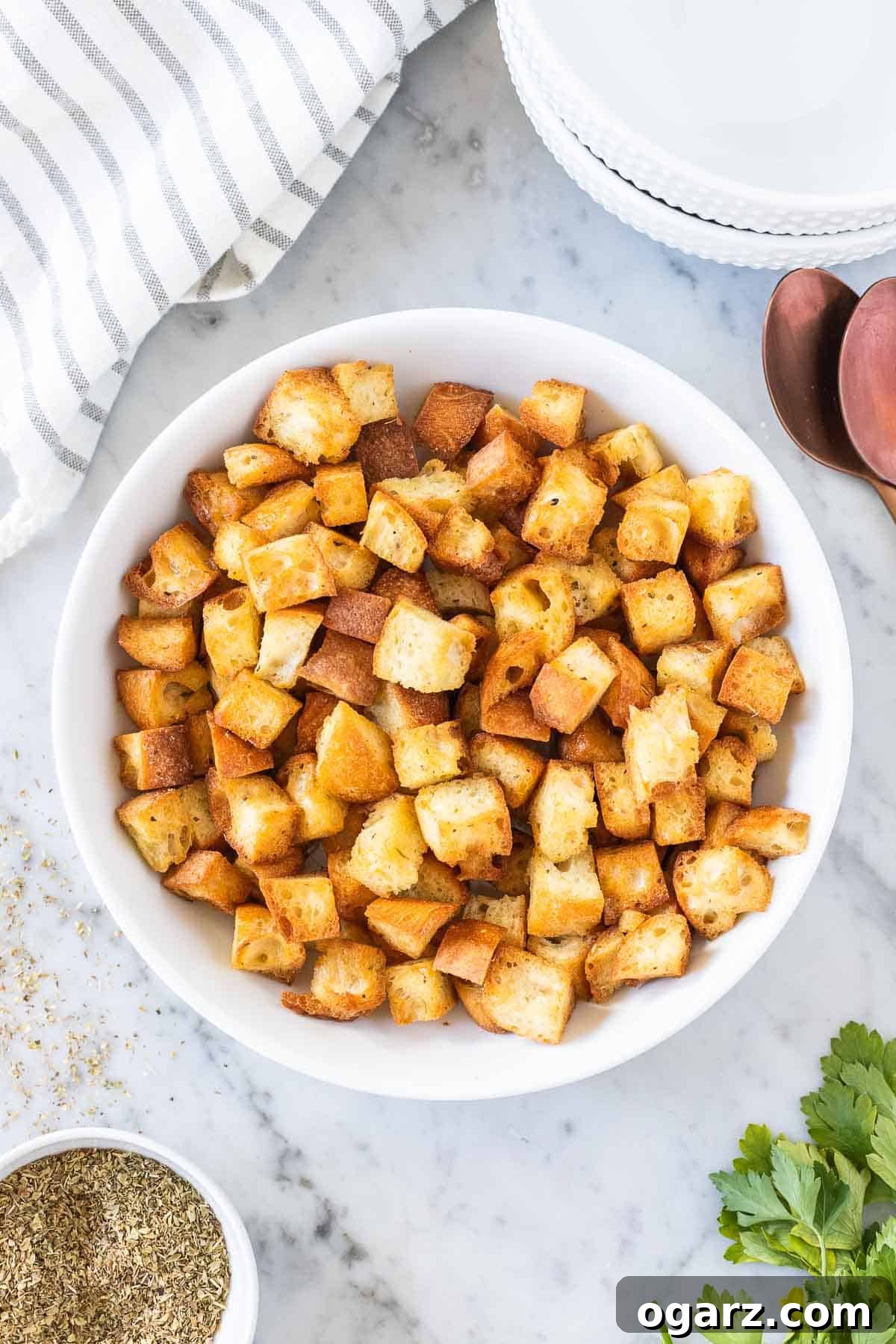 Crispy Air Fryer Croutons 2 Golden, crispy croutons in a white bowl, ready to serve, next to a spoon and a kitchen towel on a elegant marble board.