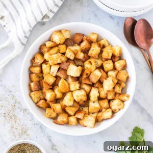 Croutons in a white bowl next to a spoon and a kitchen towel on a marble board.